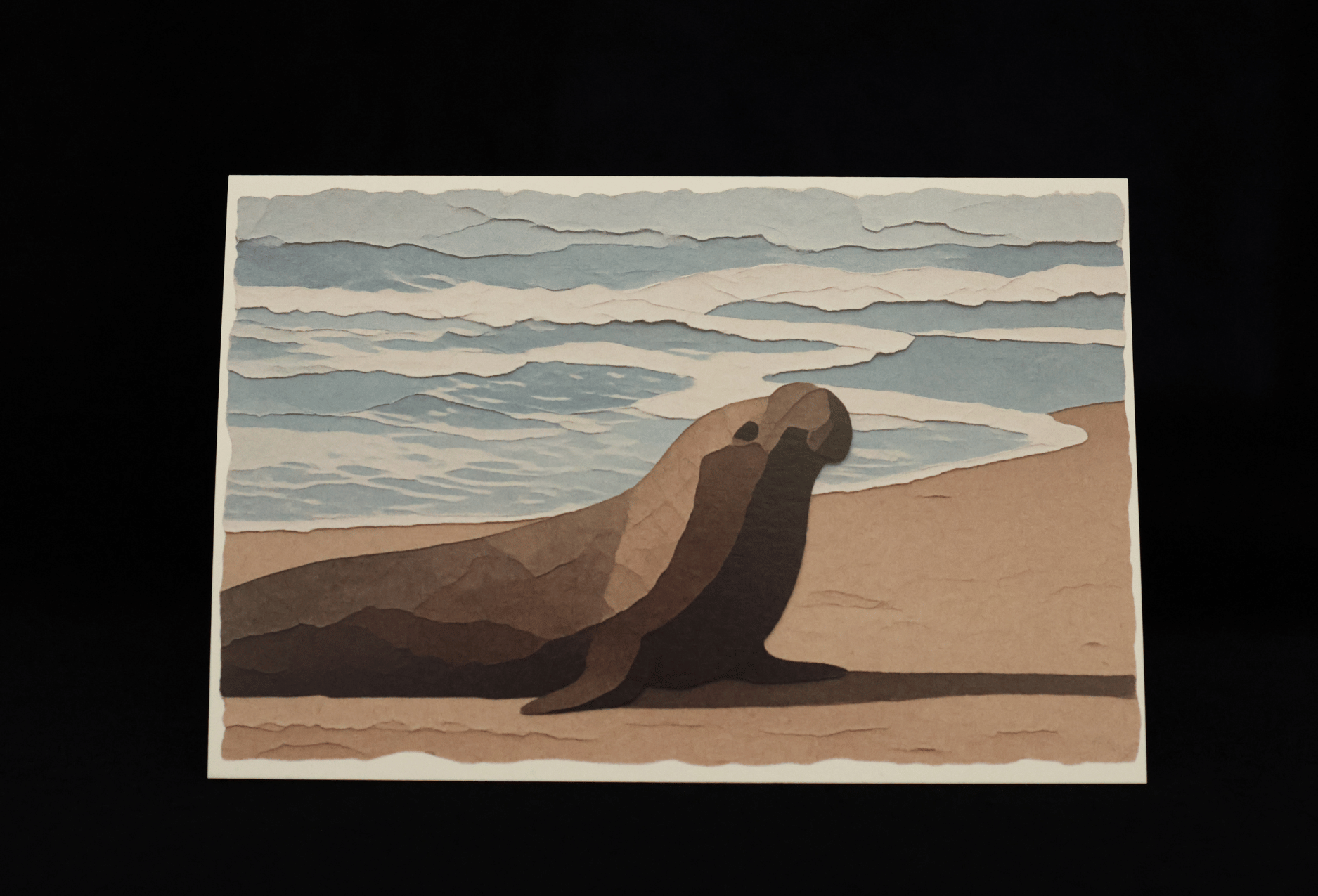 A notecard with a stylized elephant seal resting on a sandy beach with ocean waves in the background, shown against a solid black backdrop.