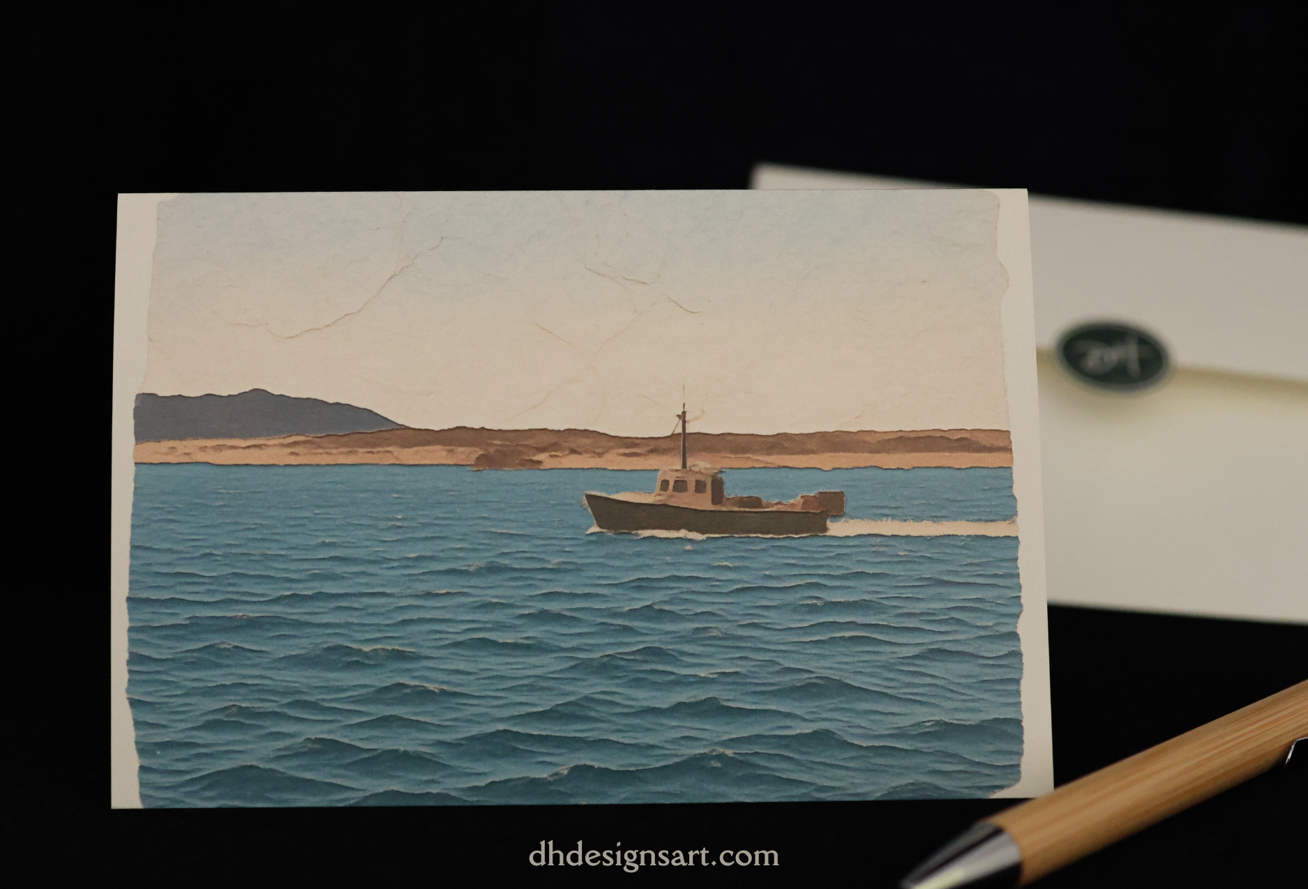 A snotecard depicting an image from Morro Bay, CA - a layered illustration of a fishing boat on blue water with a sandy shoreline under a pale sky, displayed on a black background with an envelope and pen partially visible.