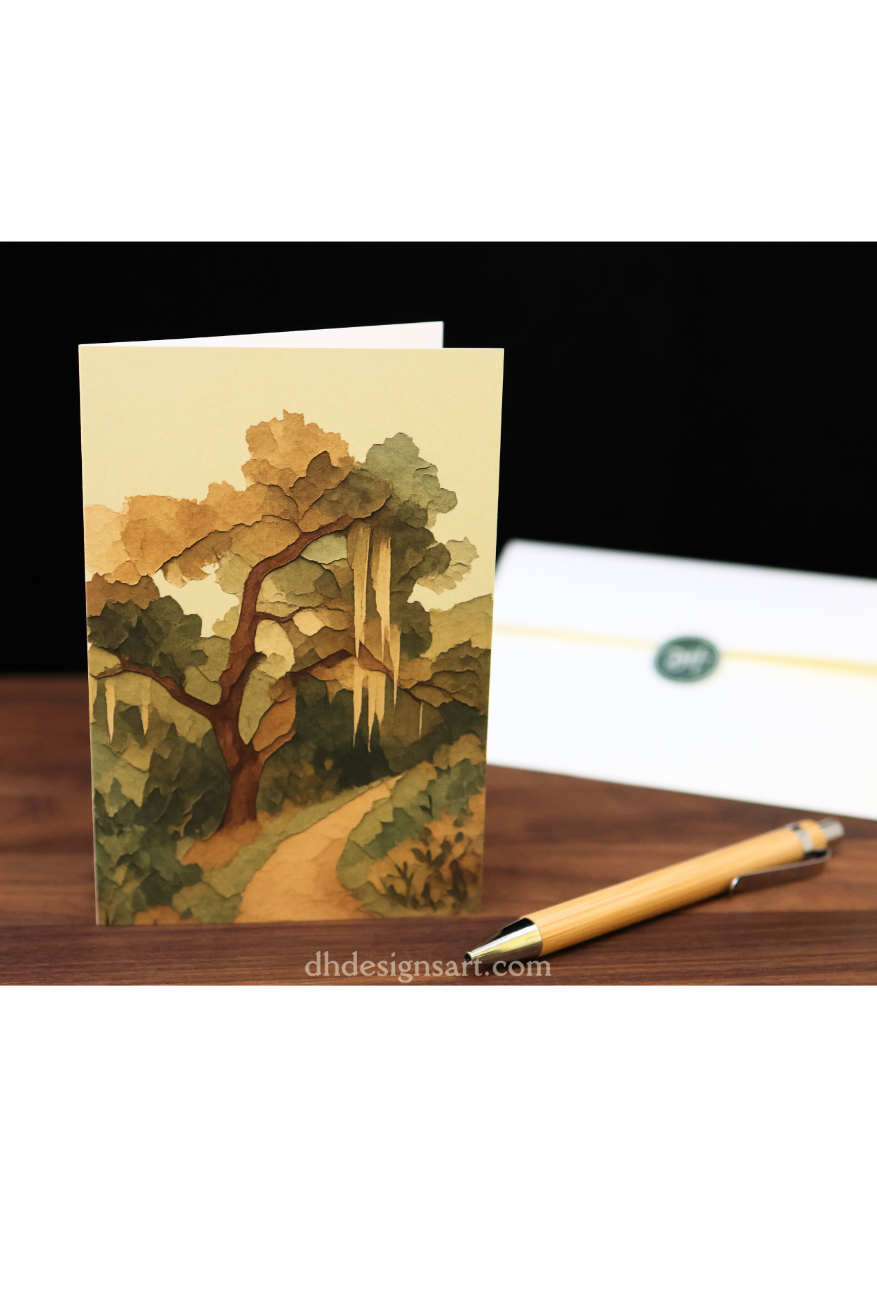 Blank notecard with an oak tree scene on a wooden desk with a pen.