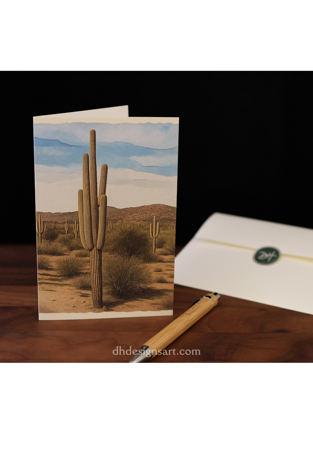 Blank notecard depicting a desert scene with a saguaro cactus set upon a wooden desk with a pen and envelope.