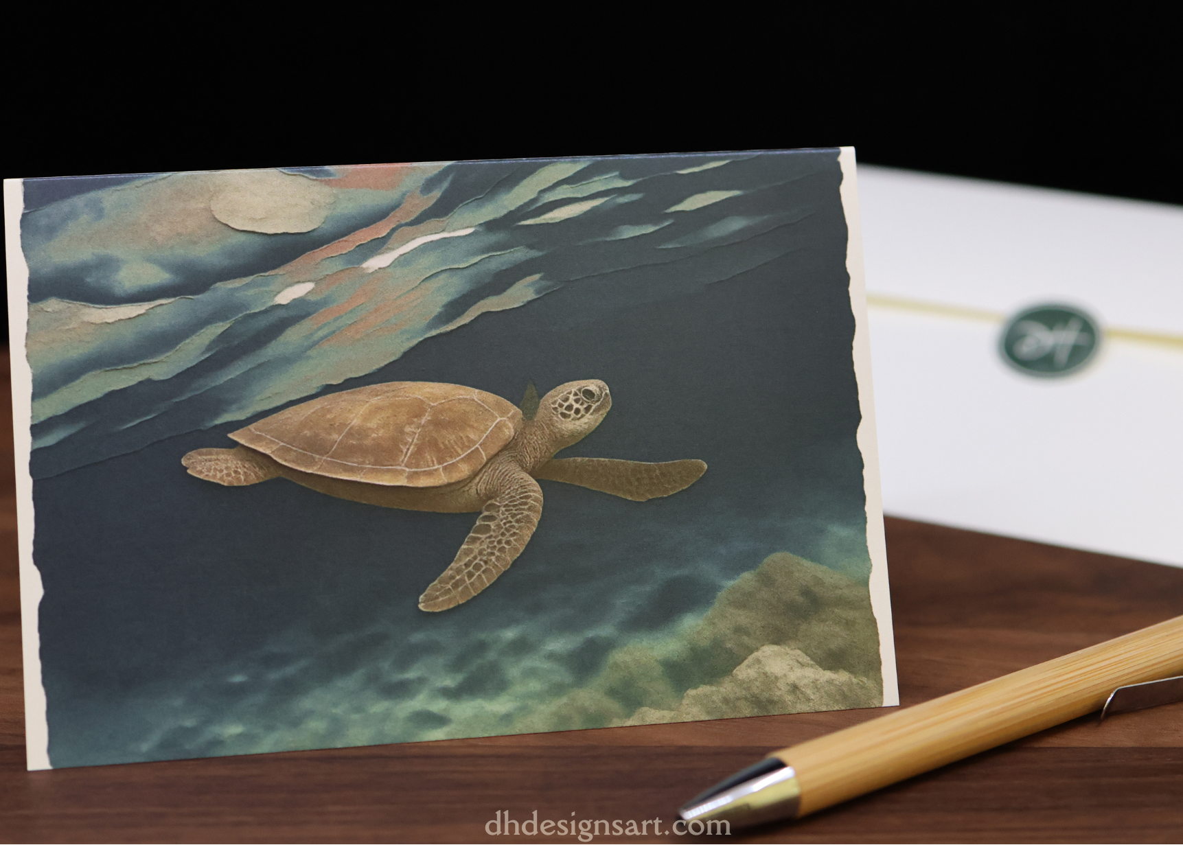 Blank notecard depicting a sea turtle swimming in dark blue water, set upon a wooden desk with a pen, and envelope.
