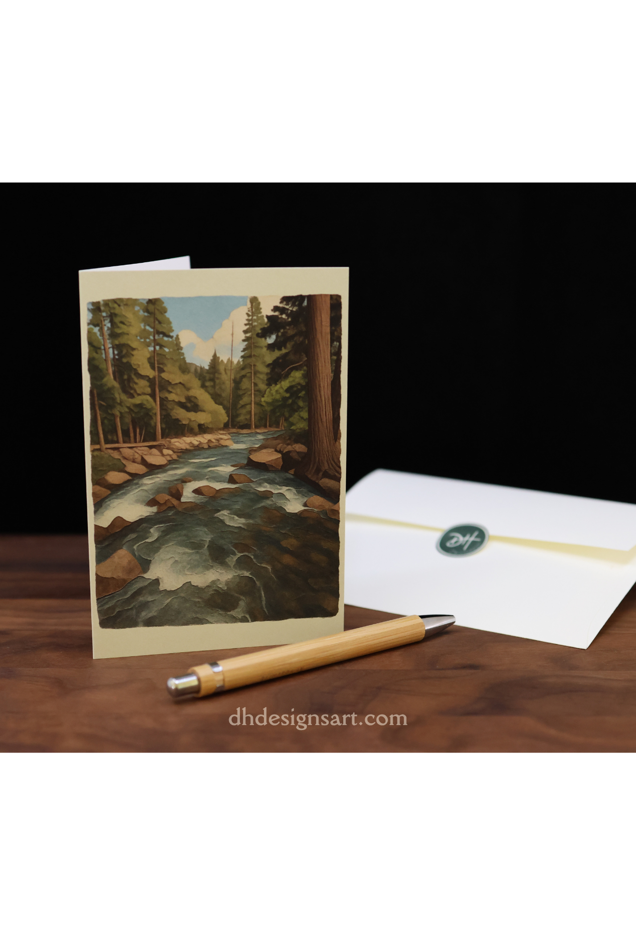 Blank notecard with a Yosemite pine forest and creek, an envelope on a wooden desk, and 'dhdesignsart.com' branding.