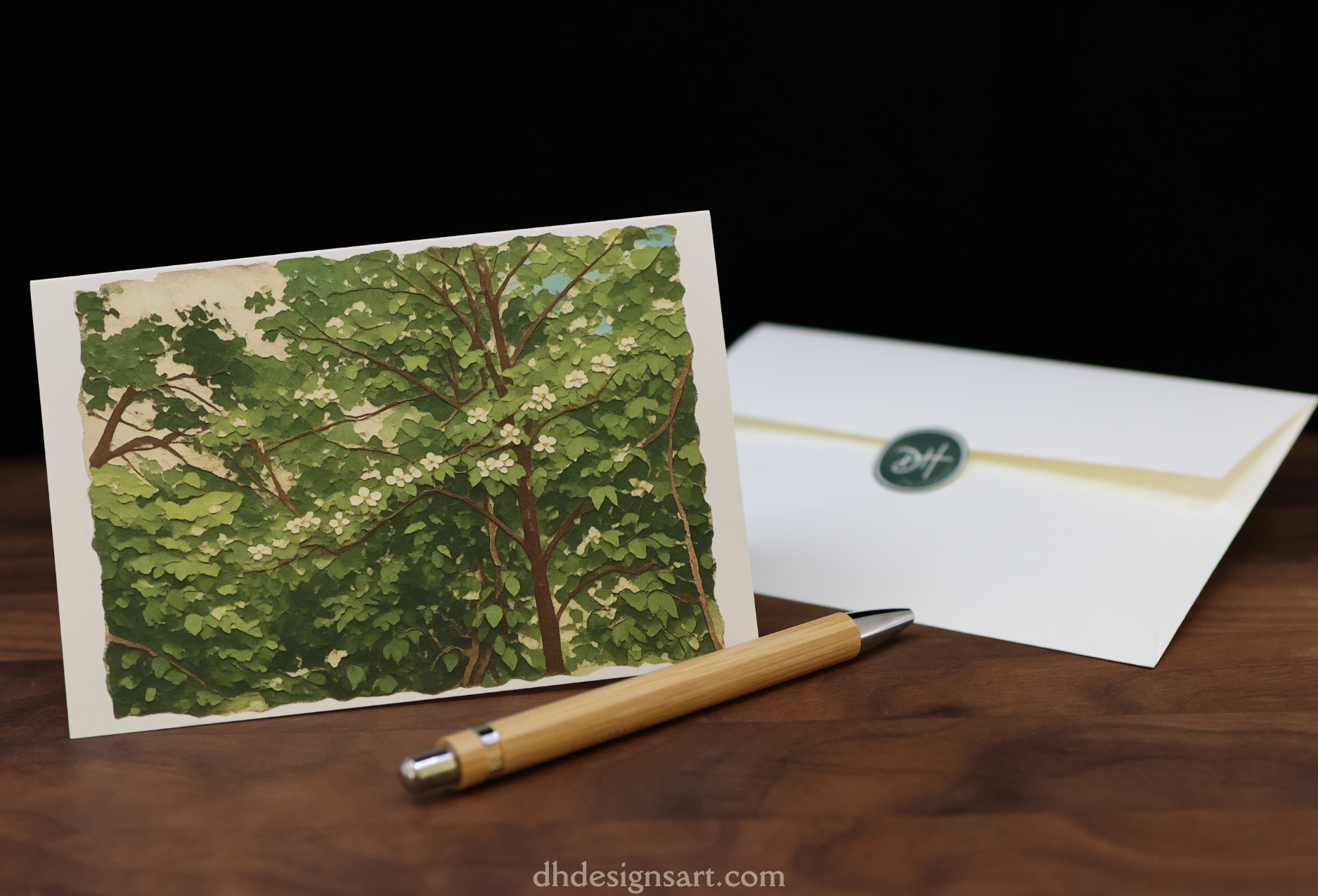 Blank notecard with a blooming dogwood tree design, pen, and envelope on a wooden desk.